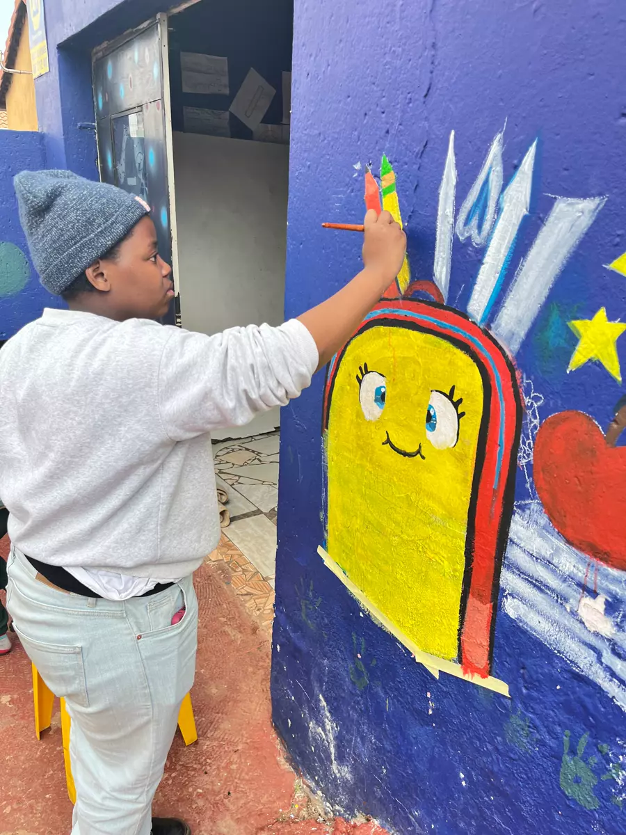 A young person painting a mural on a blue wall