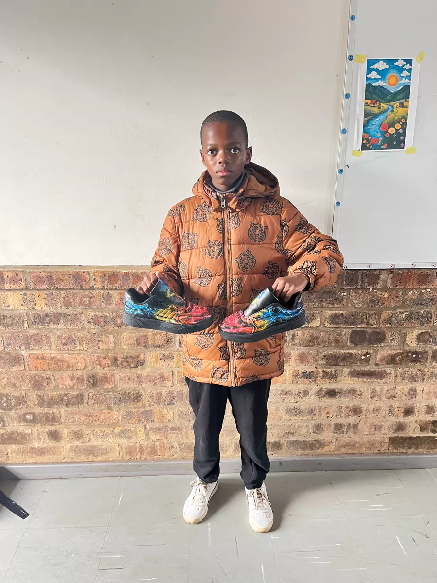 A young boy proudly holding up custom-painted sneakers he created
