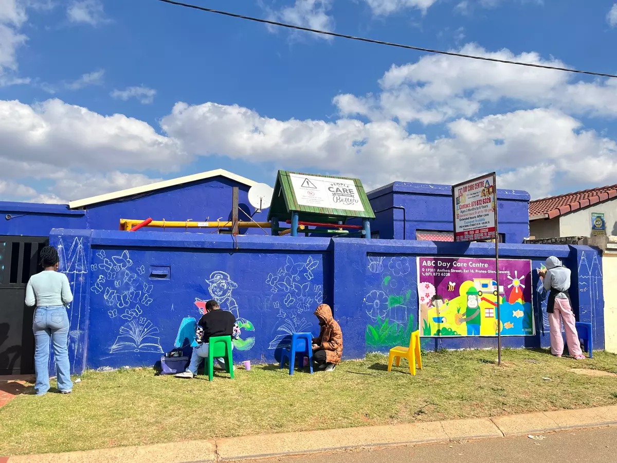 Daycare exterior with chalk drawings and people painting on a blue wall