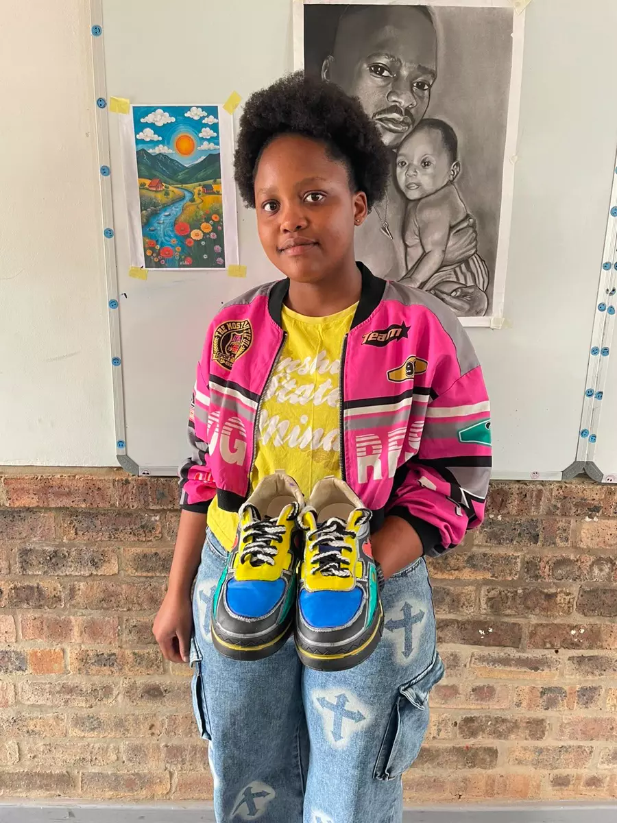 A young woman holding up a pair of colourful custom sneakers she designed