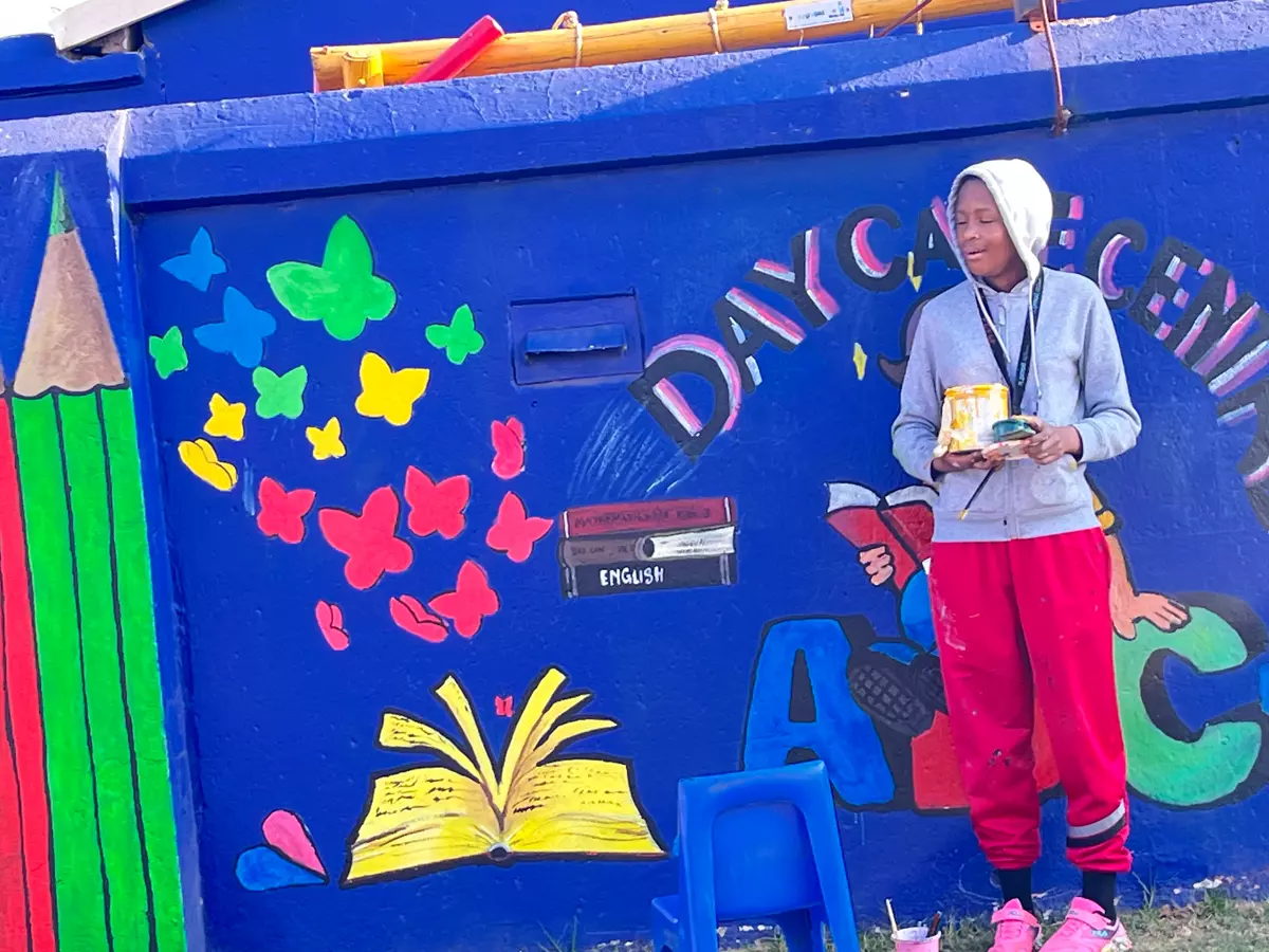 A young person standing in front of a blue wall with a colourful mural