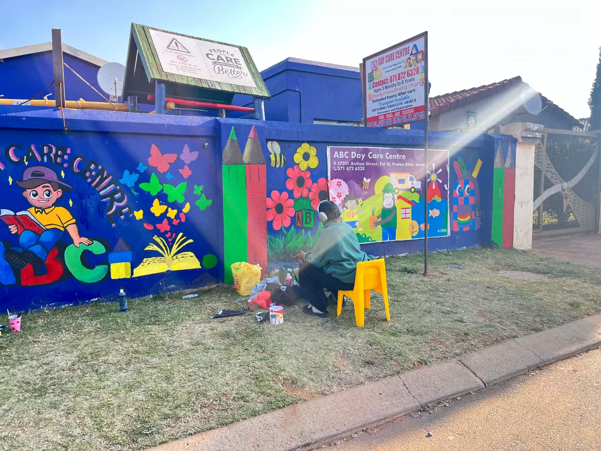 An artist painting a colourful mural on a blue wall in front of a suburban street