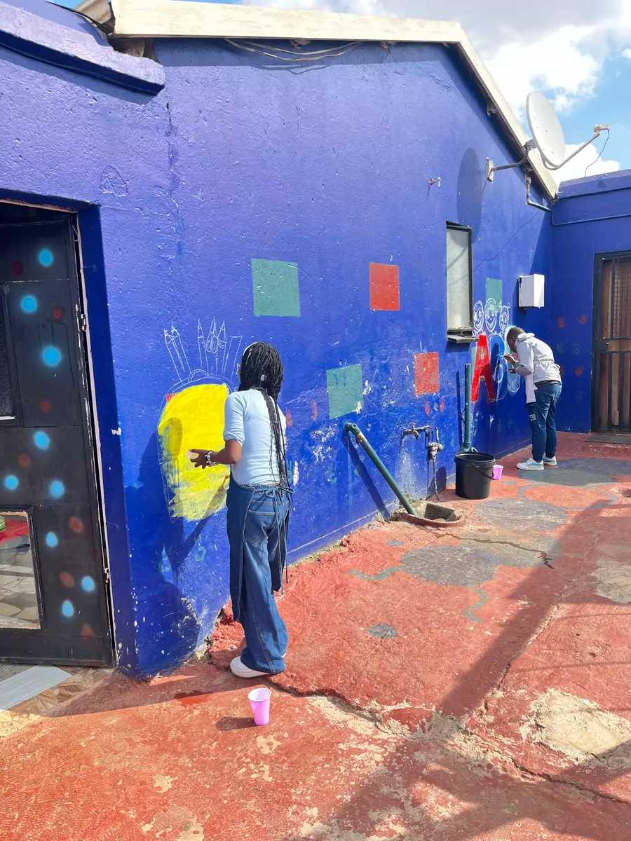 Two people painting a mural on a blue wall in a courtyard