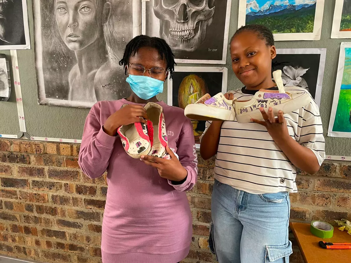Two young women holding up custom-painted sneakers in an art studio