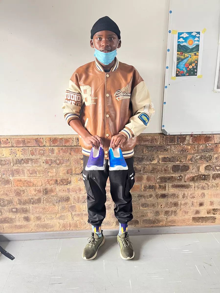 A young man holding up two shoes in front of a brick wall