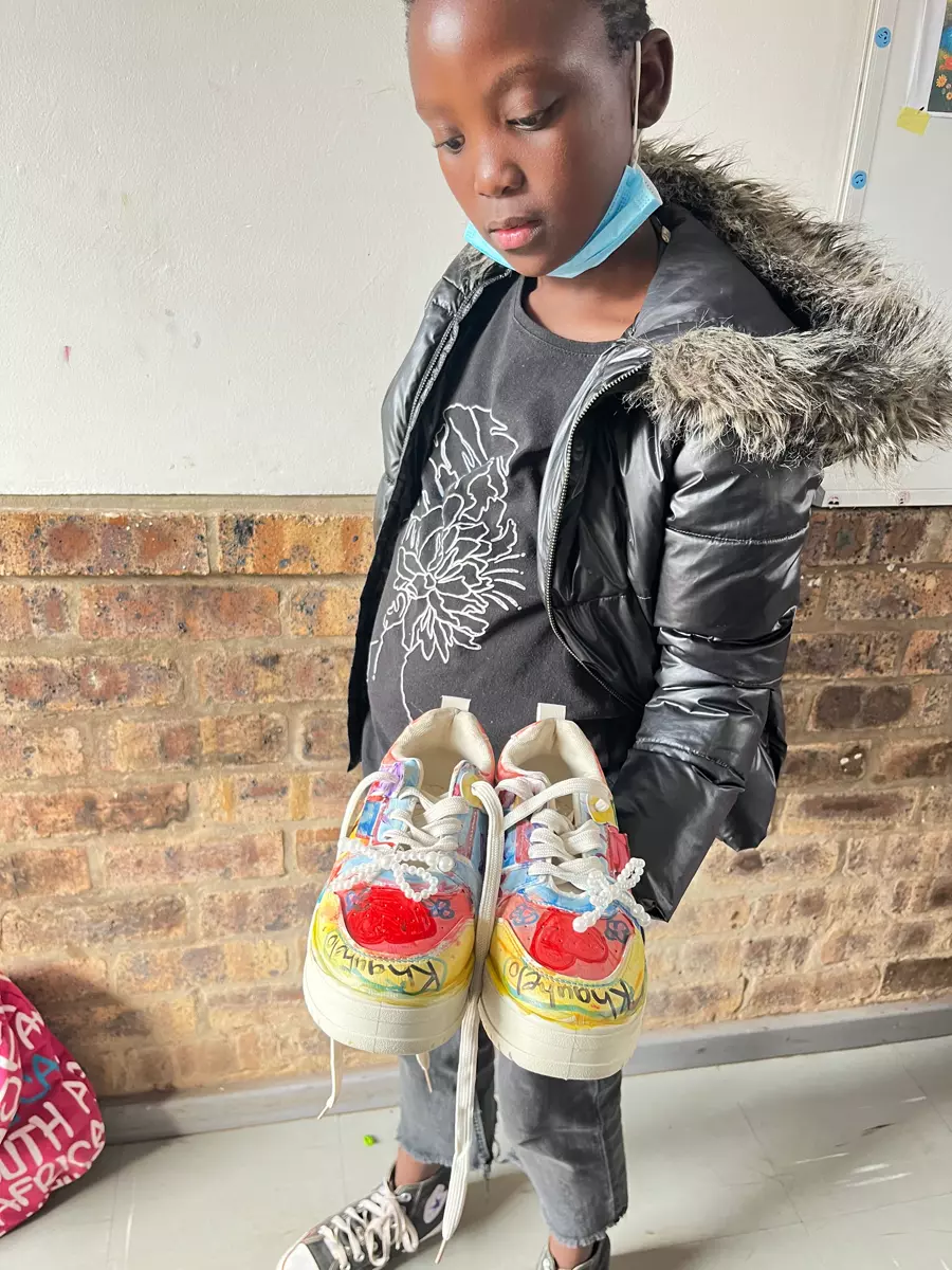 A young girl holding up a pair of custom hand-painted sneakers