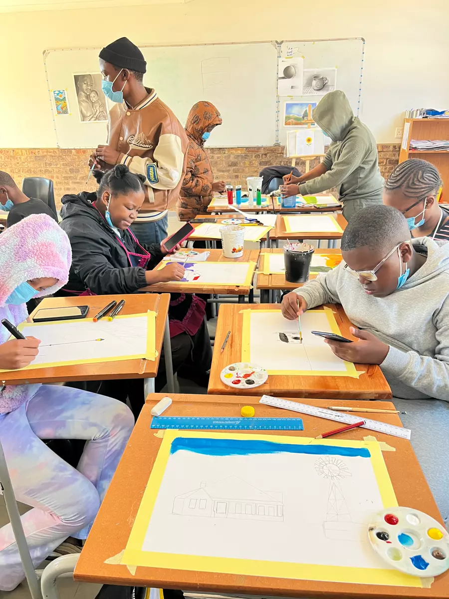 Teenagers and young adults engaged in art classes, seated at wooden desks painting and drawing