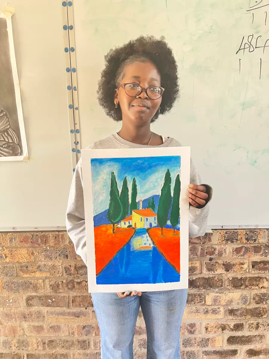 A woman holding up a colourful painting of a landscape with a house and cypress trees
