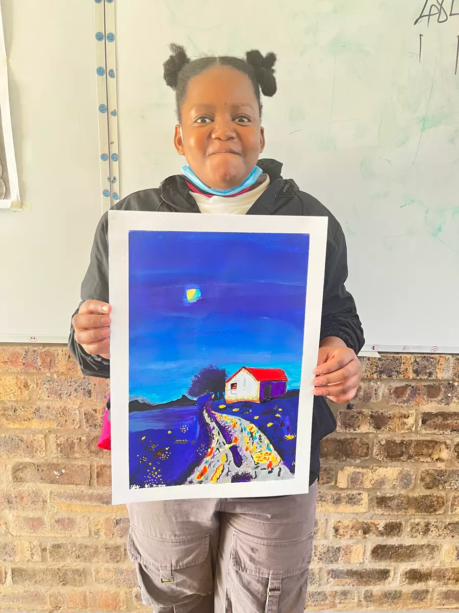 A young girl holding up her painting of a landscape