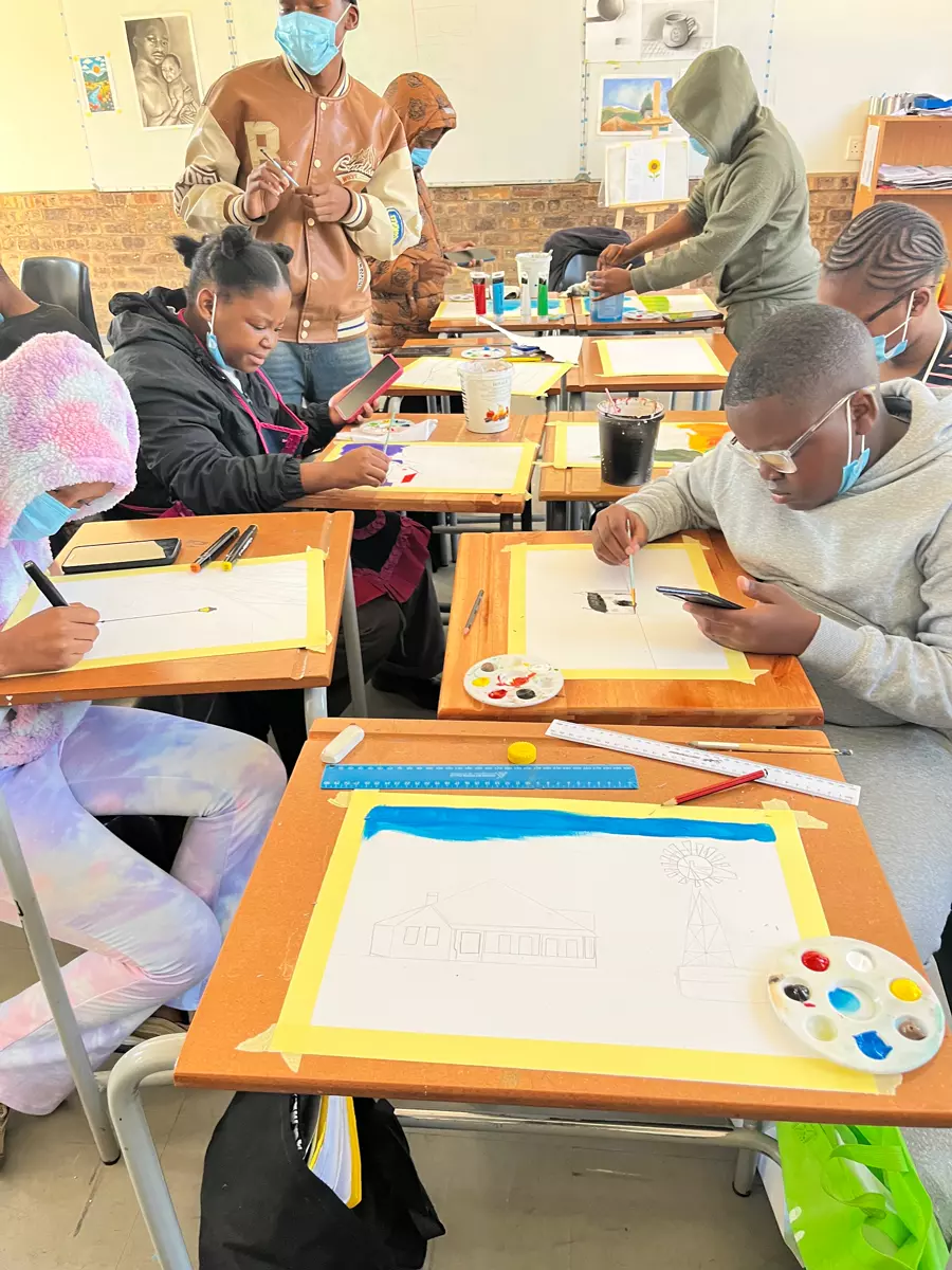 Young students focused on art projects in a classroom, drawing and painting at wooden desks