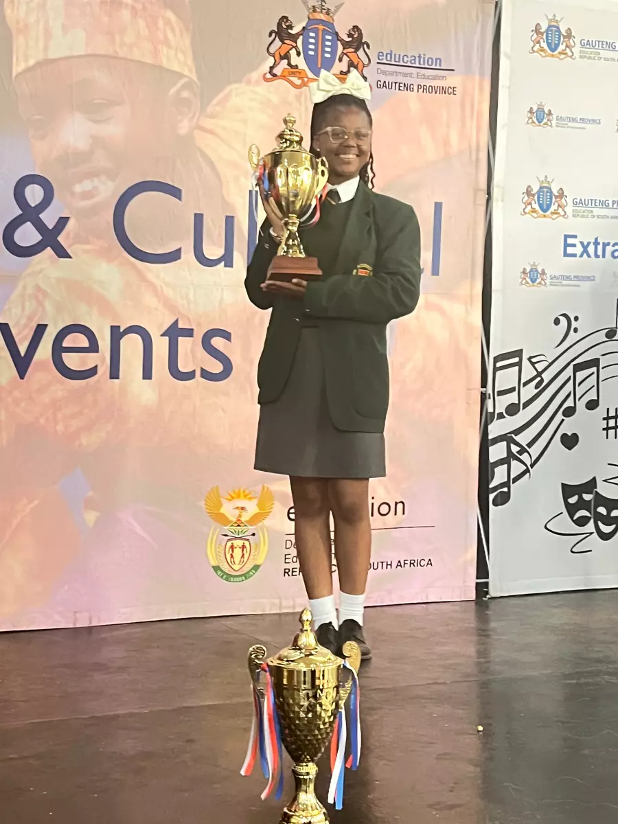 A young girl in a school uniform holding a gold trophy on stage