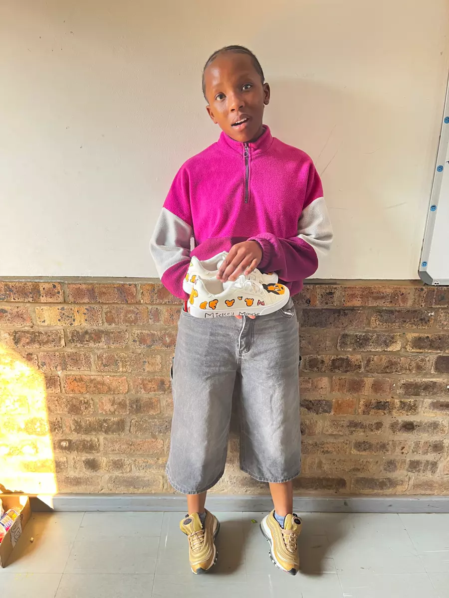 A young person holding up custom-painted white shoes