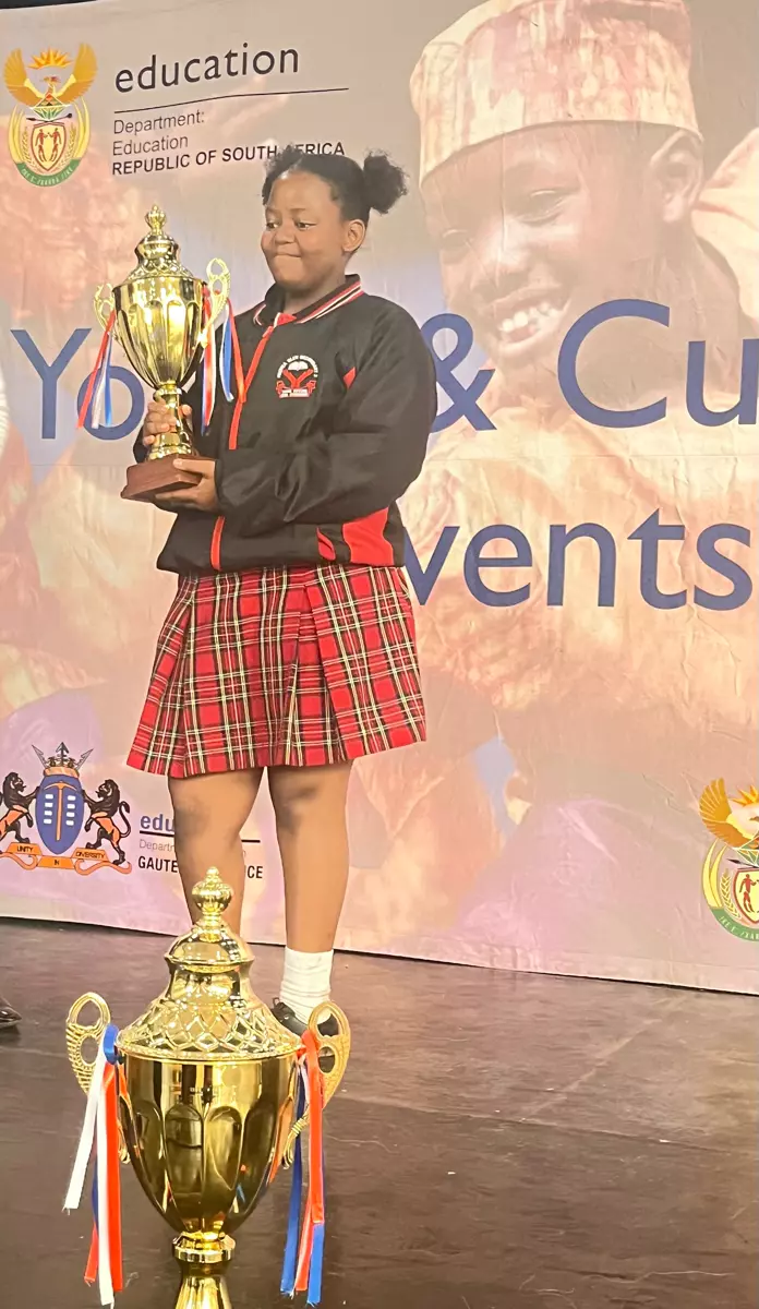 A young girl holding a trophy in front of a banner