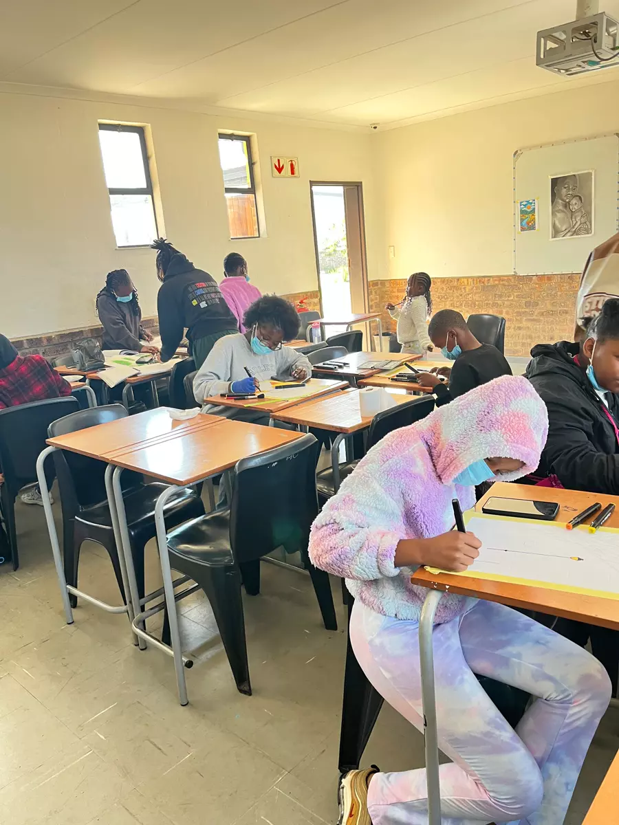 Students focused on art projects at wooden desks in a DFSOA classroom